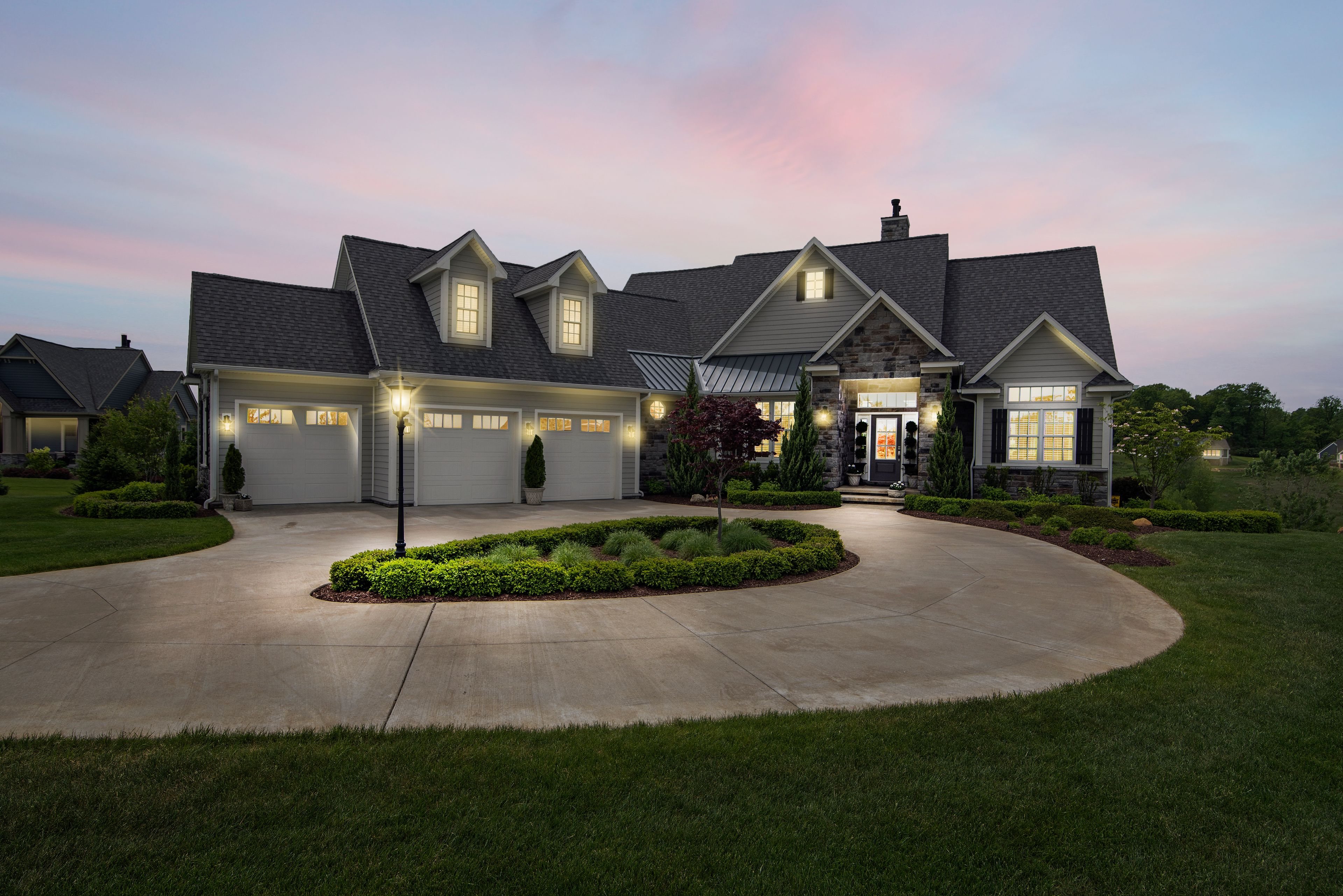 Luxury craftsman home glowing at twilight with a circular drive